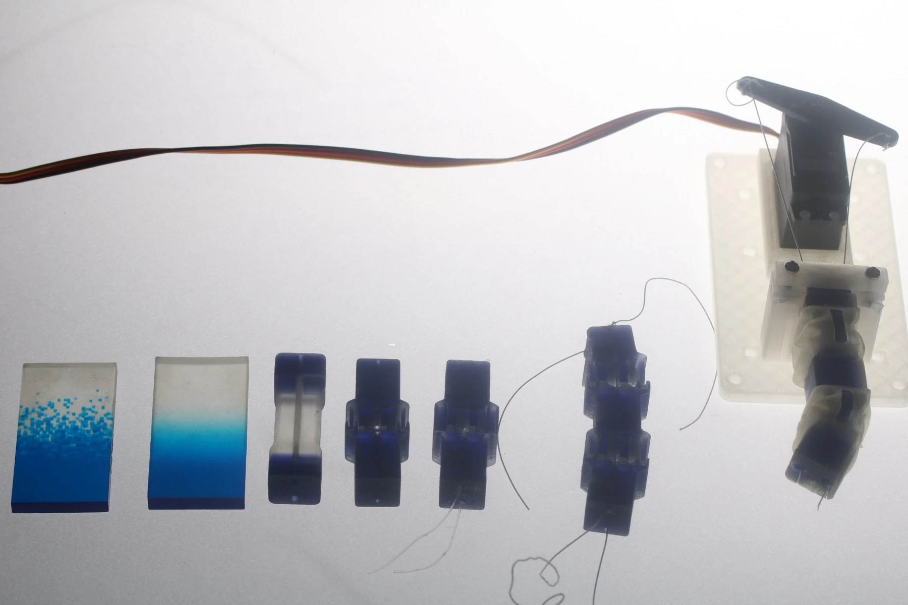A row of blue material samples and printed finger joints alongside a servo-driven finger